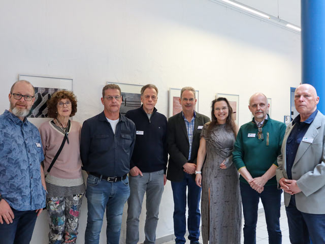 Zu sehen sind die Künstler:innen der Gruppe "Deichfotografen" vor einigen ihrer Bilder im Lichthof der vhs.