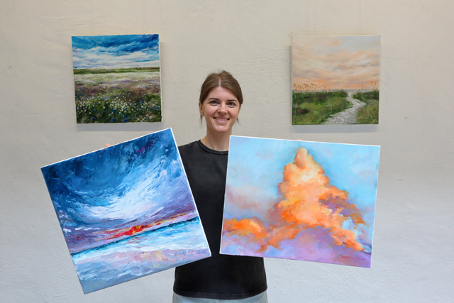 Künstlerin der neuen Ausstellung: Kateryna Konovka mit zwei Bildern in den Händen und zwei im Hintergrund im Lichthof der vhs Delmenhorst